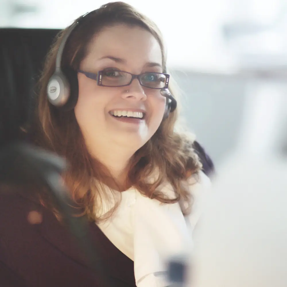 tab-kategorie-service-01.png Junge Frau mit Headset und Brille lächelt in die Kamera