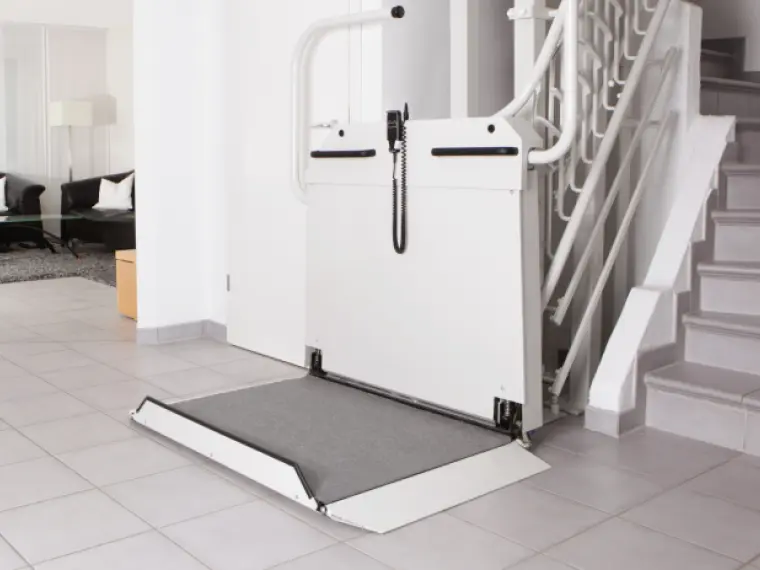 homelift-6.png Ein weißer Rollstuhllift parkt am unteren Ende einer Treppe
