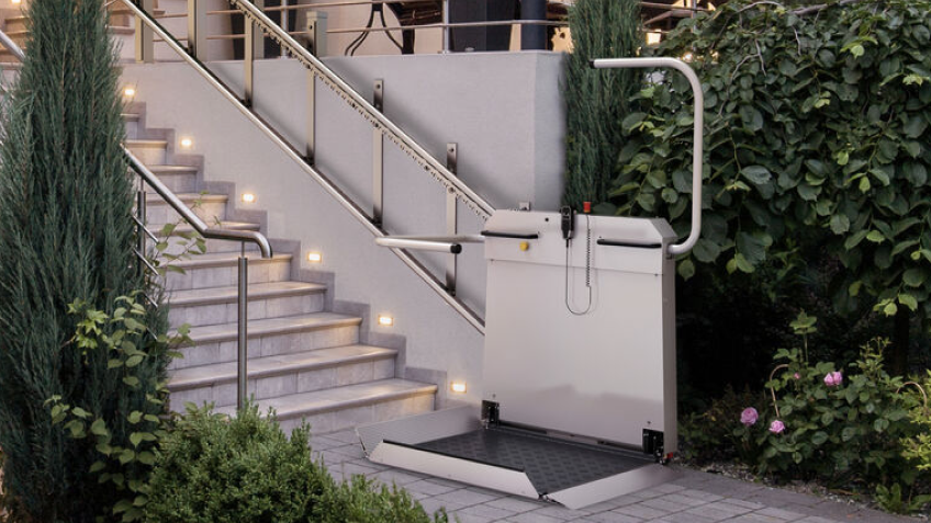 markenteaser-sanitrans.png Plattformlift für Rollstuhlfahrer von sani-trans am Ende einer beleuchteten Außentreppe