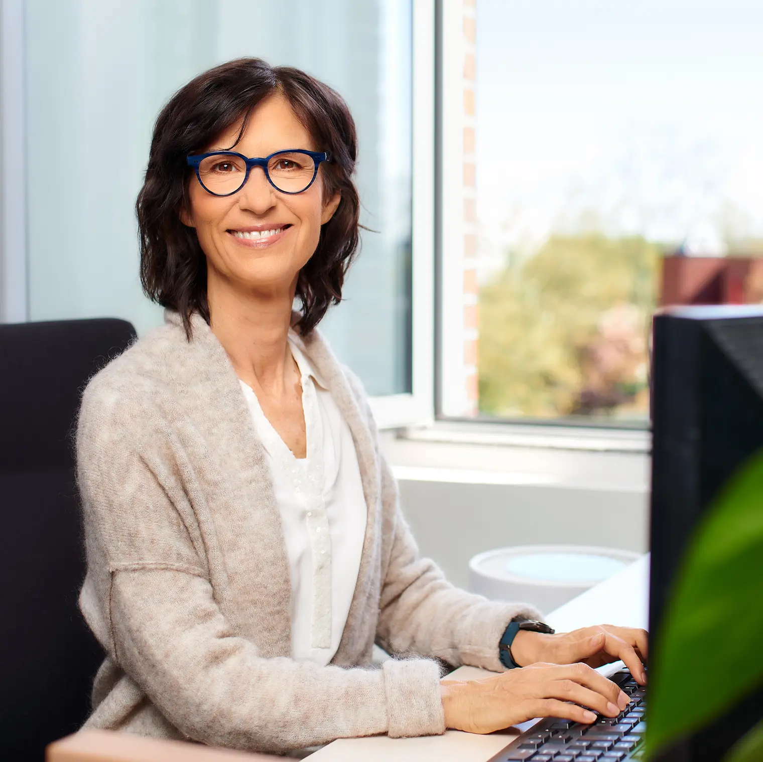 Dunkelhaarige Frau mit Brille am Computer sitzend